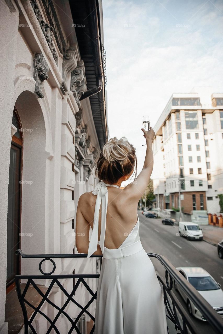 Happy bride in white wedding dress hold glass of wine outside