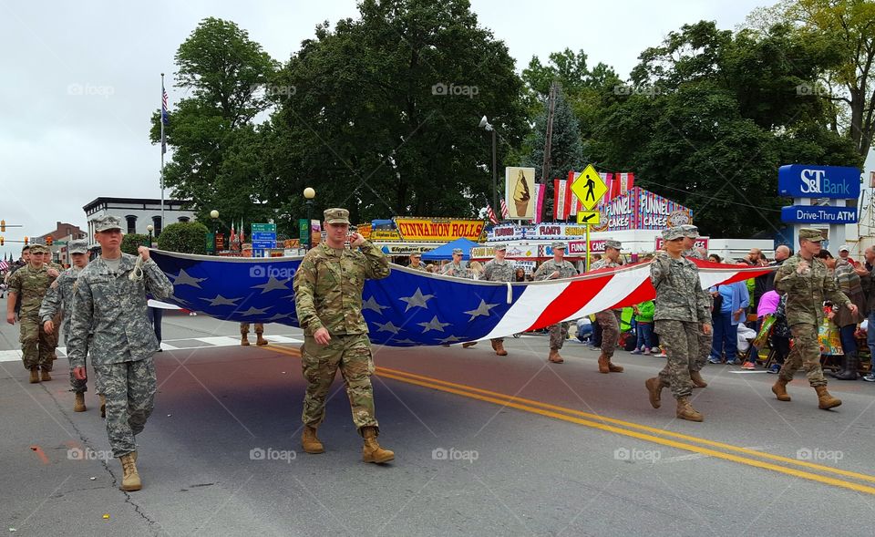Servicemen in camouflage gear carry the United States flag during a fall festival parade.