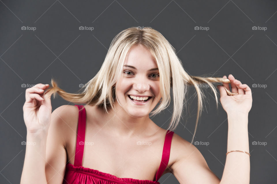 The happy girl to twist hair in hands on gray background