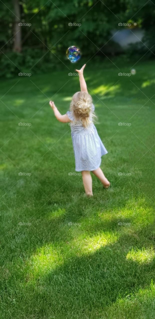 reaching for floating bubbles while running barefoot in the grass