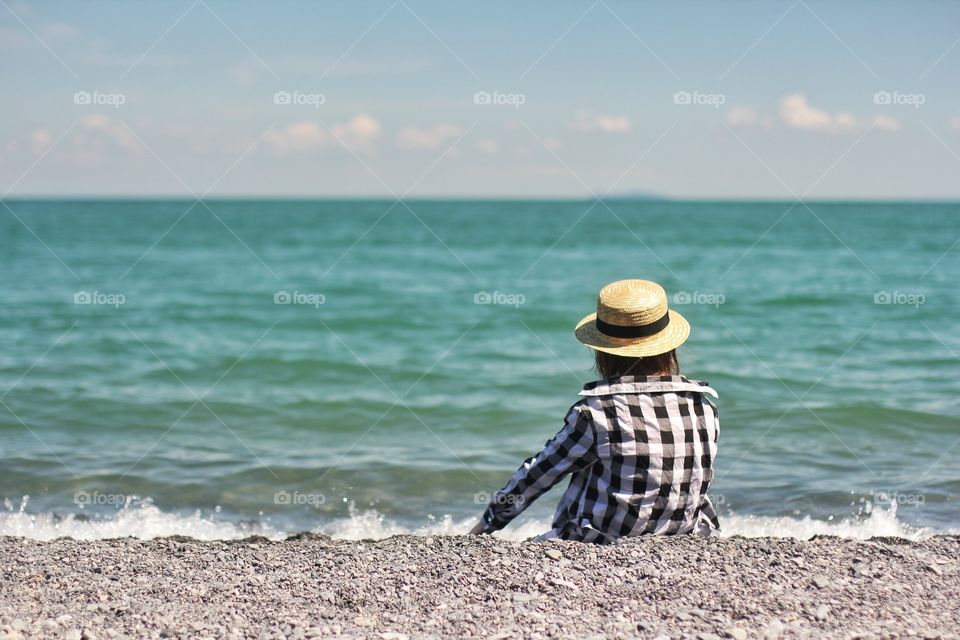 Little girl sits on the shore and looks into the distance