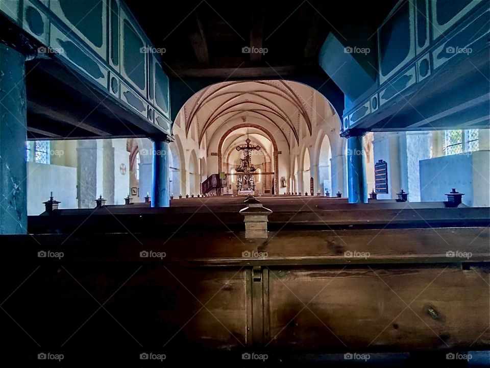 This is the interior of the medieval parish church of “Altenkirchen” on the island “Rügen” in “Western Pomerania”, Germany: the balcony, benches, center aisle and glowing in gold tones the altar with central crucifix. 2024. Hypnotic Productions