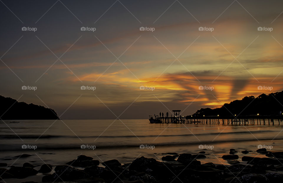 The sunset behind the island in the sea and the shadow of the tourists on the wooden bridge at Koh Kood, Trat in Thailand.