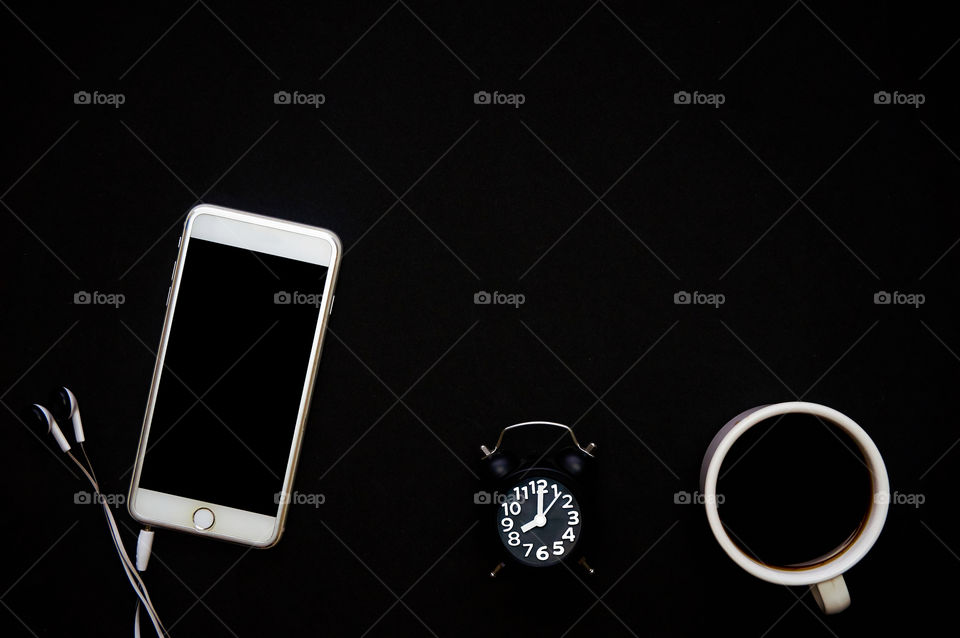 Smartphone and coffee, alarm clock on black background with copy space 
