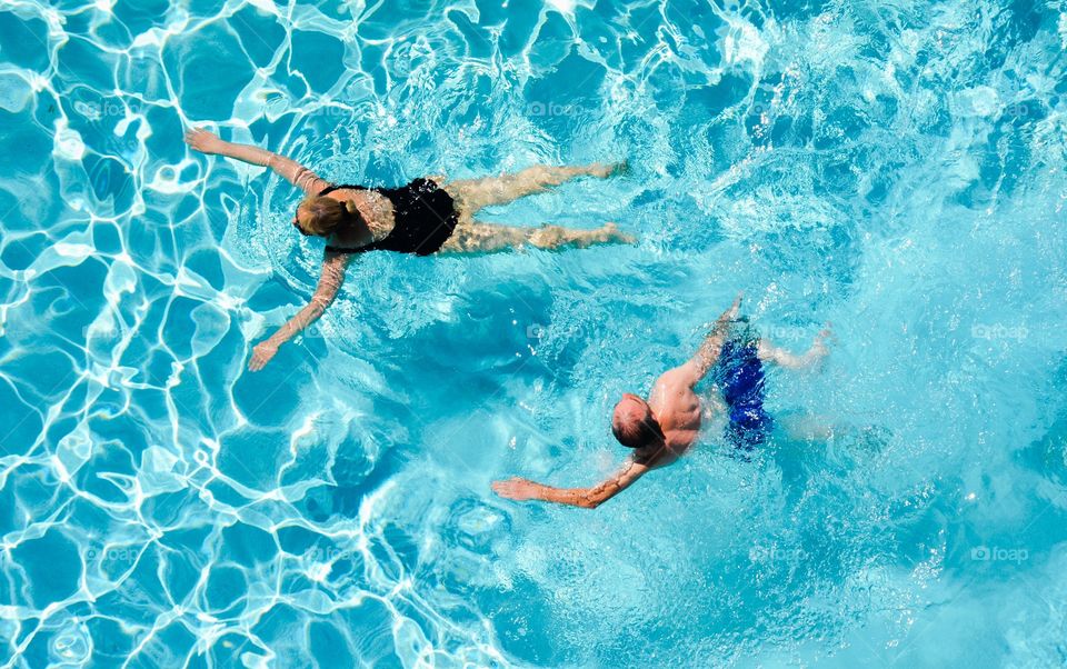 Two adults swimming in a cool blue swimming pool.