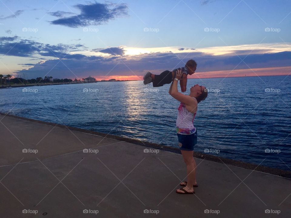 Woman playing with boy at sea side during sunset