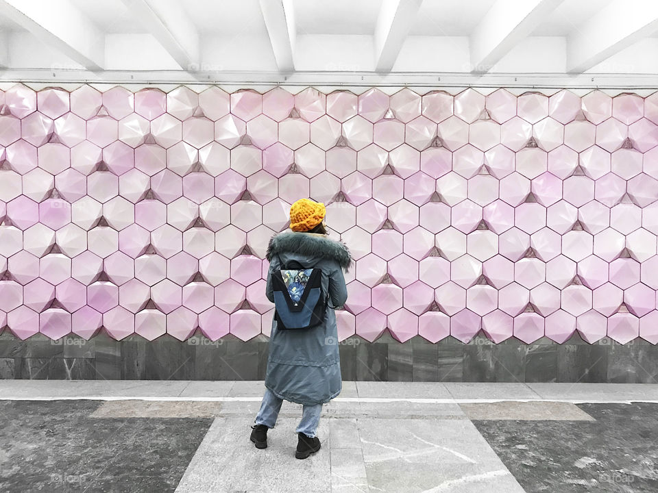 Young woman with a backpack standing in front of pink wall with geometric pattern 