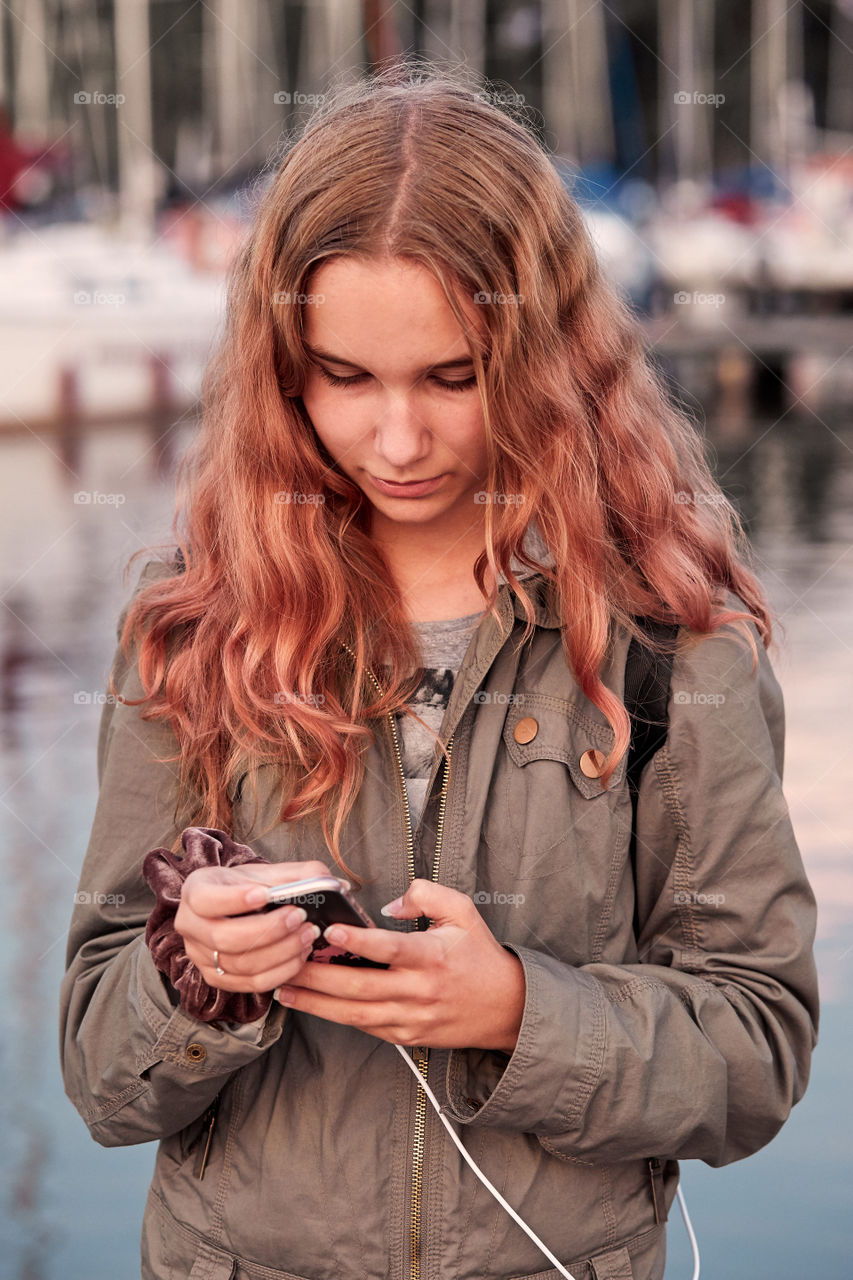 Young woman using mobile phone smartphone standing on a pier over a lake. Candid people, real moments, authentic situations