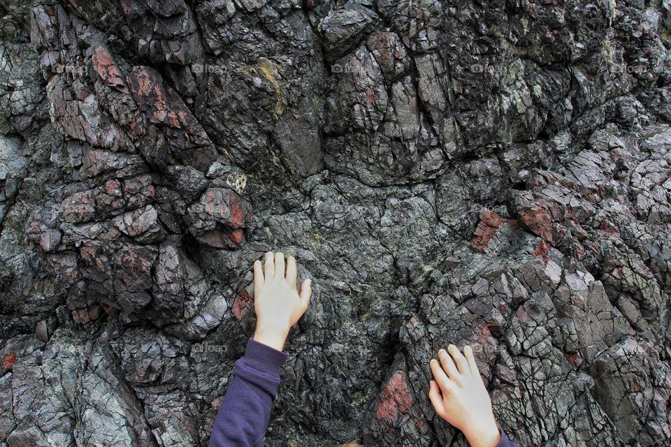 Hands climbing over harsh, granite rock on a cliff face.