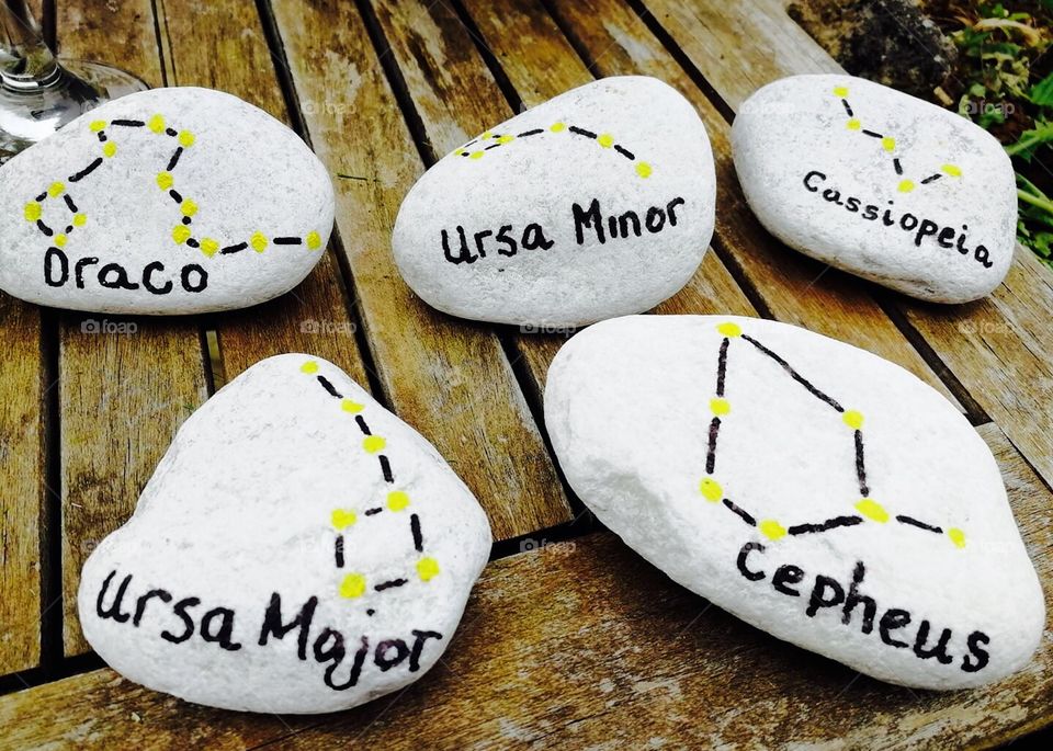 5 five hand painted rocks of constellations in black and yellow on a wooden table