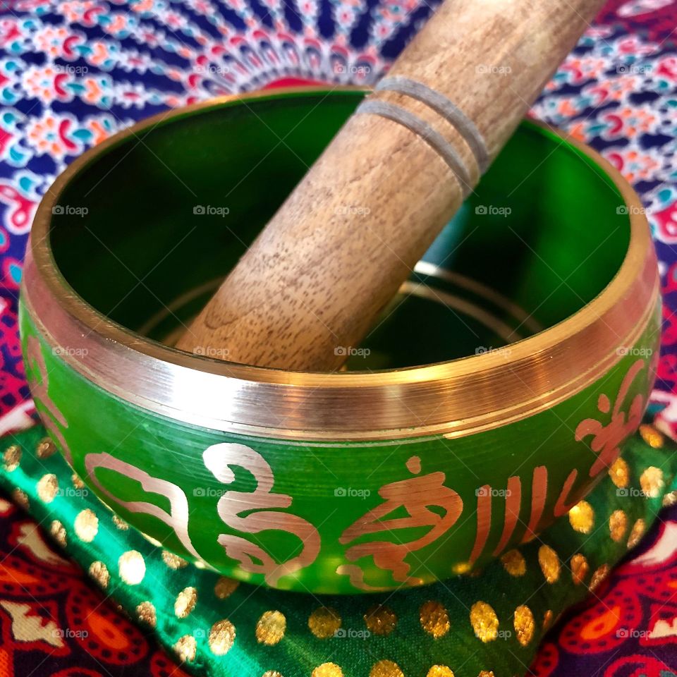 Green Tibetan Singing Bowl with a wooden striker on a vibrant rainbow mandala meditation cushion balances heart and soul.