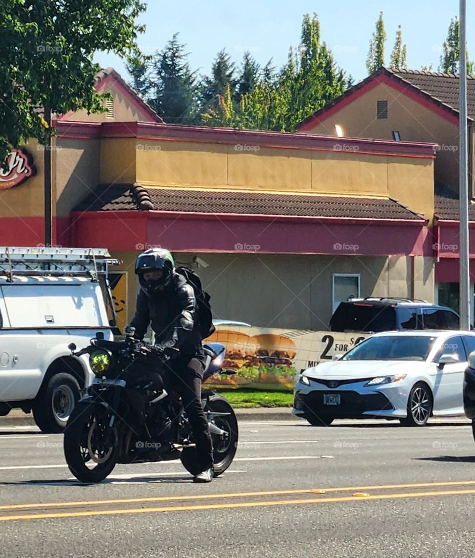 man in blackwesring a helmet riding a black bicycle in Oregon afternoon commuter traffic