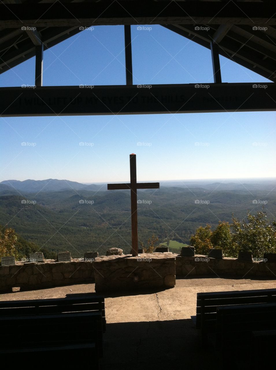A cross silhouetted in front of a panoramic mountain scene, taken from a stone chapel.