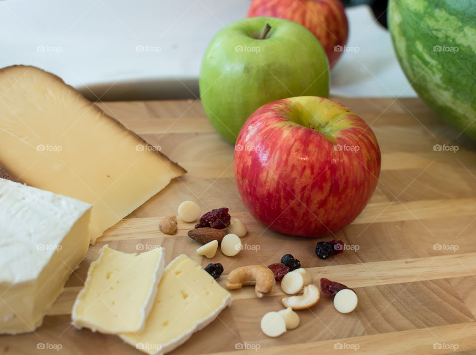 Row of fresh red and green apples on wood table with healthy trail mix with cashew nuts, dried berries and sliced cheeses healthy lifestyle and eating background 