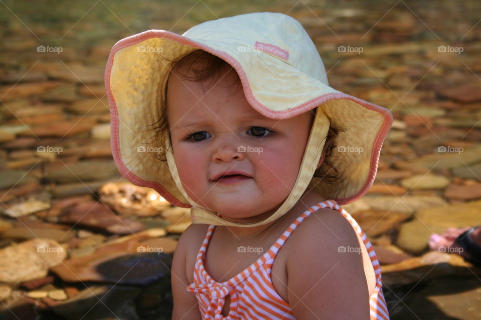 Baby girl in hat up the river.