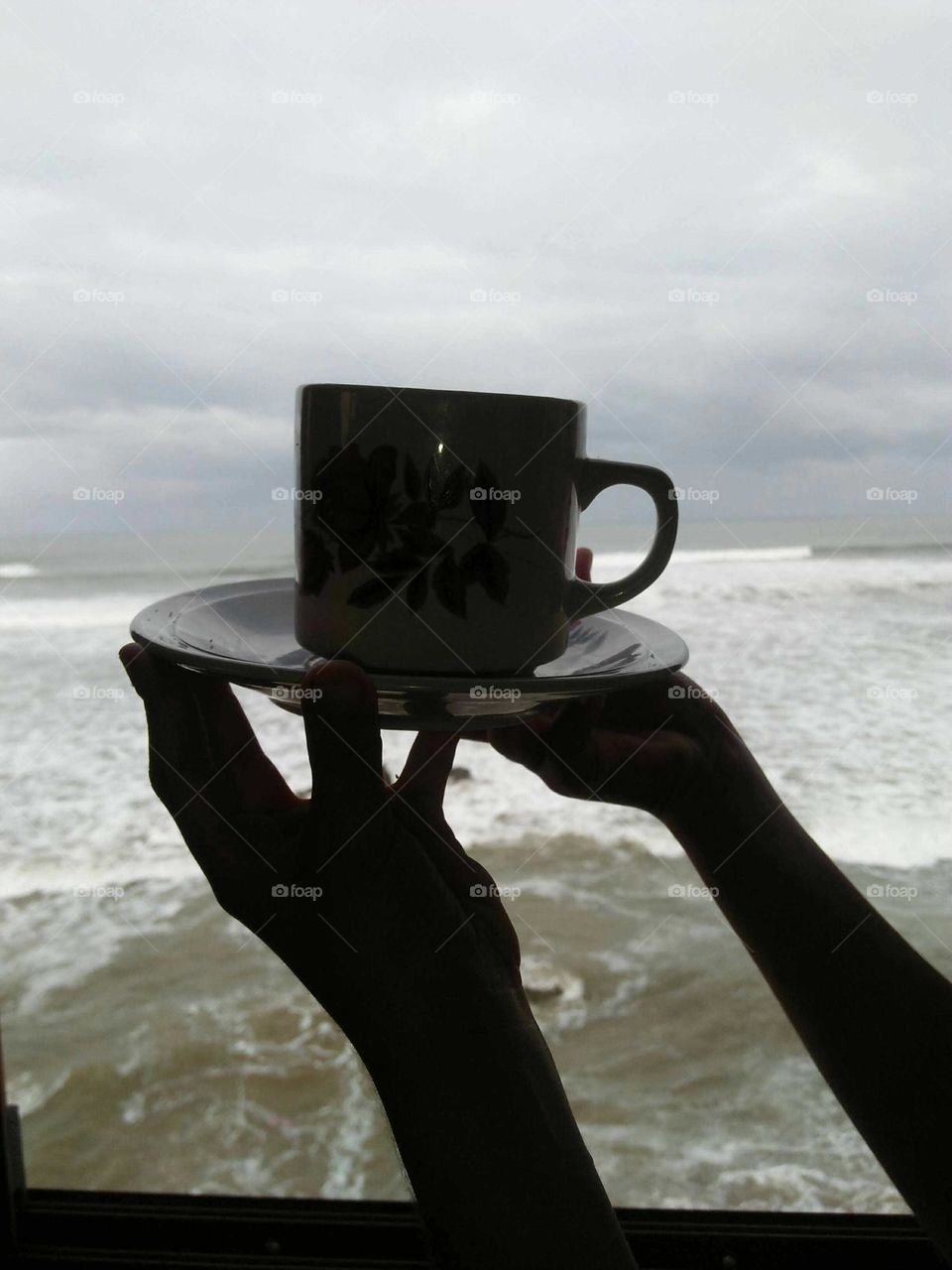 Hands holding a cup of coffee and view to the sea.