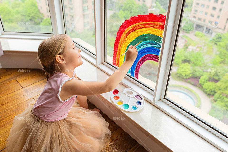 Happy kid drawing rainbow on window during coronavirus Covid-19 quarantine 