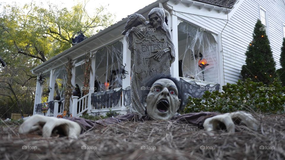 A Halloween decoration of a zombie crawling out of a graveyard at an old farmhouse.