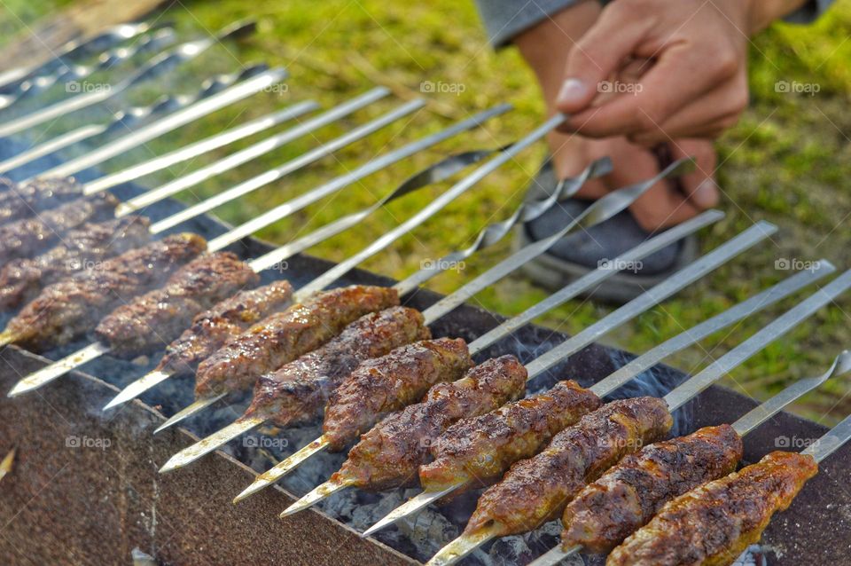 the hand turns over the meat dish being prepared on the grill. meat put on skewers is cooked on coals.