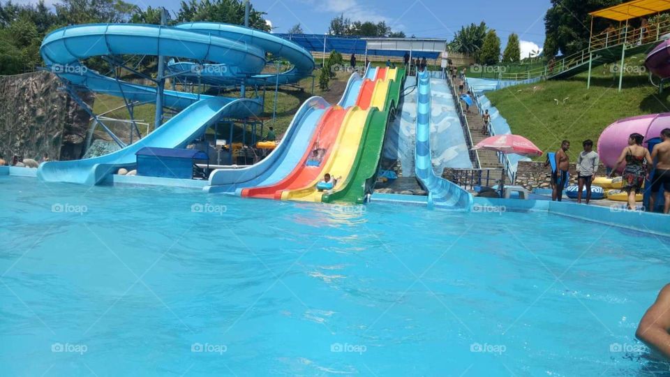 swiming pool has a rainbow slider with rotating slider with a blue water in a mountain