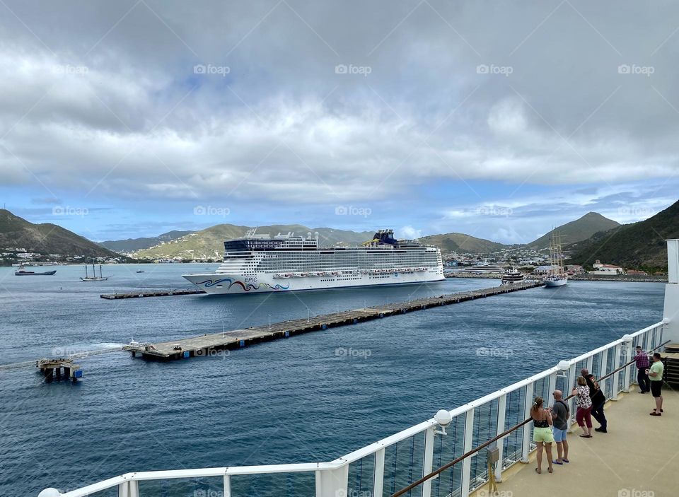 People standing at a railing of a cruise ship and looking towards another cruise ship docked in the harbor at Saint Martin