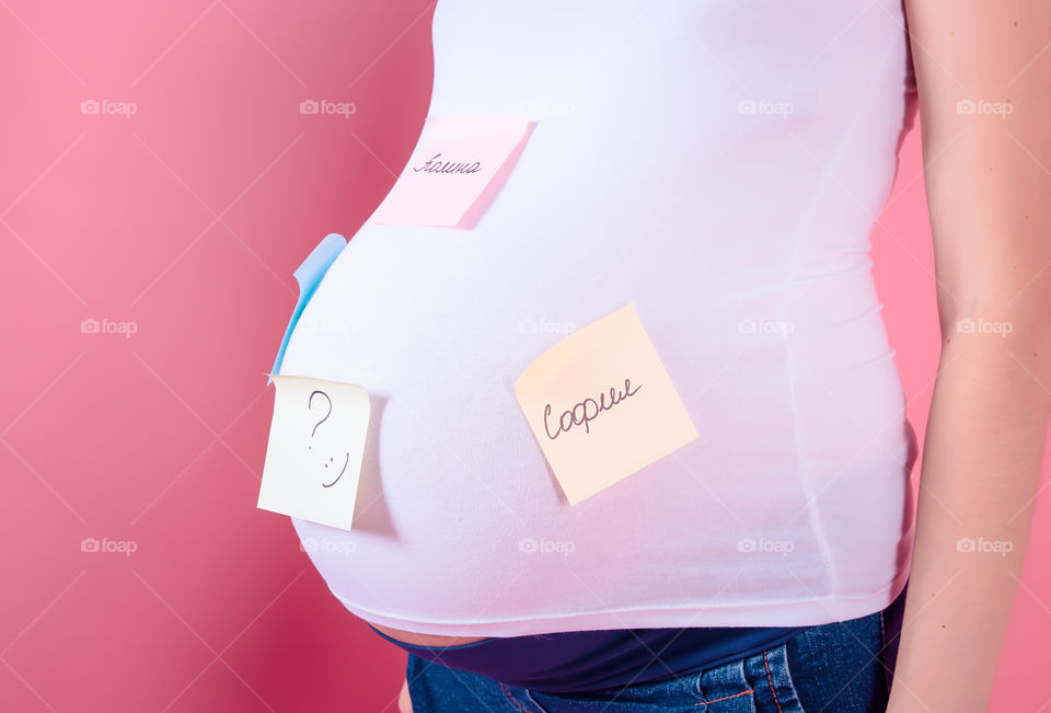 Baby names of female baby. Cropped image of pregnant woman with baby names of belly standing on pink background