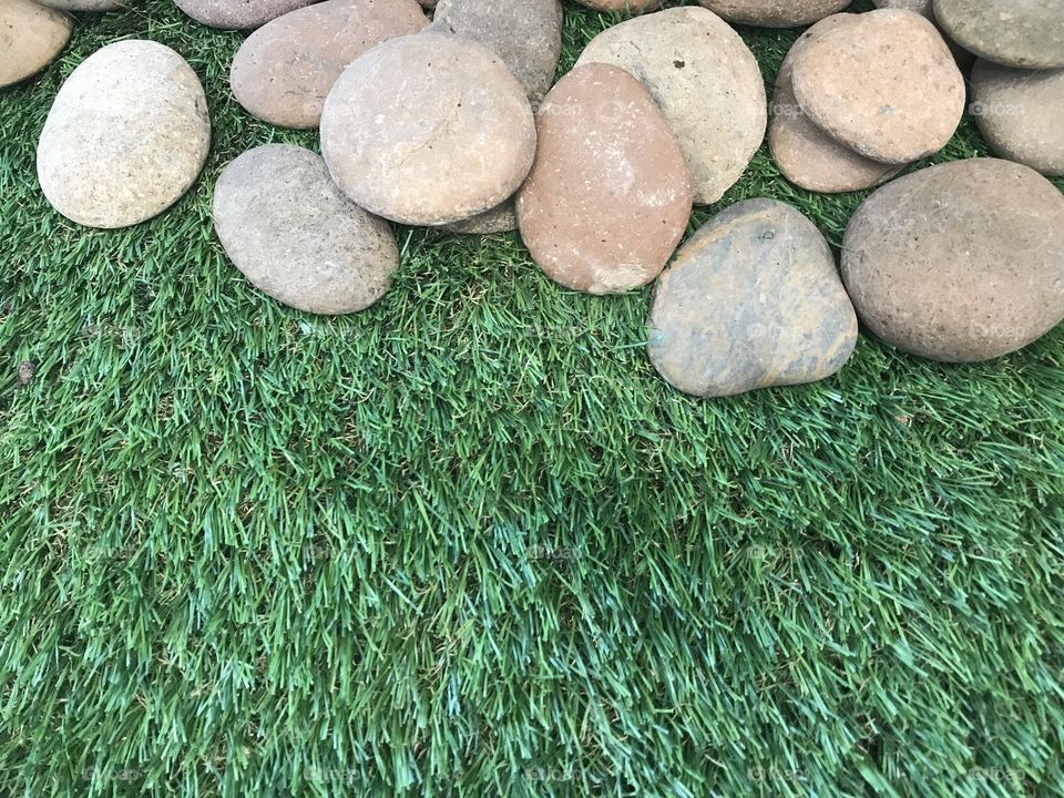 group of natural color stones at top of frame on artificial green grass, using for background
