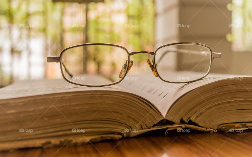 An open book and a specs or eyeglass on wooden table, on a warm sunny morning, side view close up. Education or Holiday Concept. Isolated background in selective focus, shallow depth of field