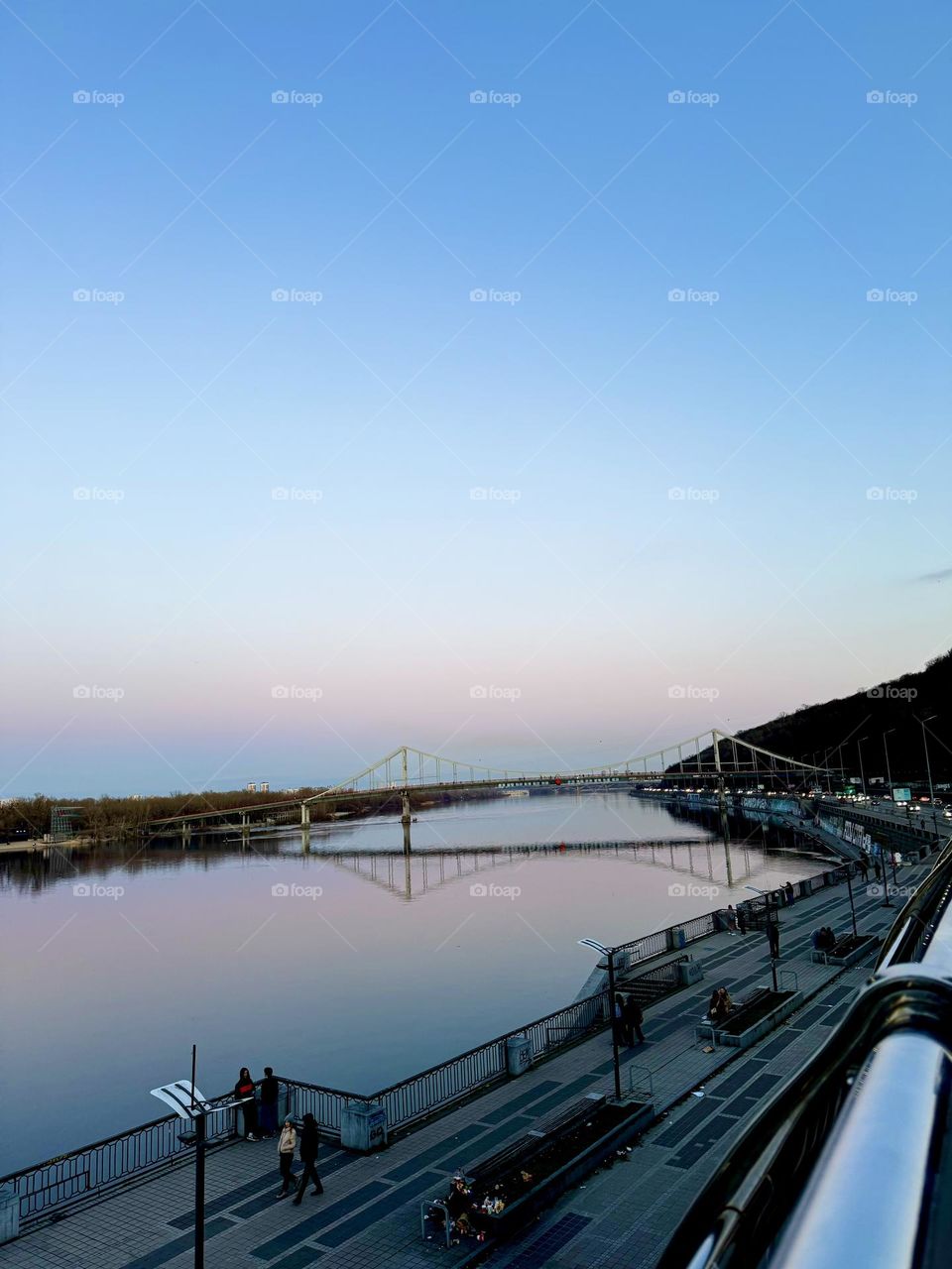 Закат над рекой Днепр в Киеве, величественный мост окутан в оранжевые оттенки солнца, создавая неповторимую атмосферу спокойствия и красоты в сердце столицы Украины 