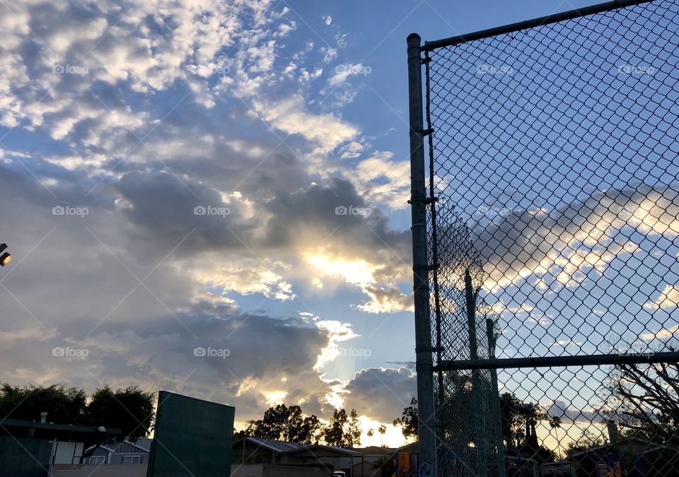 Sunset, dark clouds, blue sky & chain length fence.