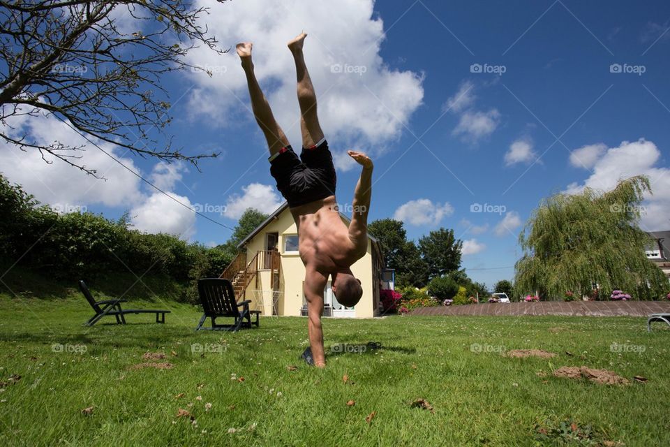A young man doing a one hand handstand yoga pose on a green field 