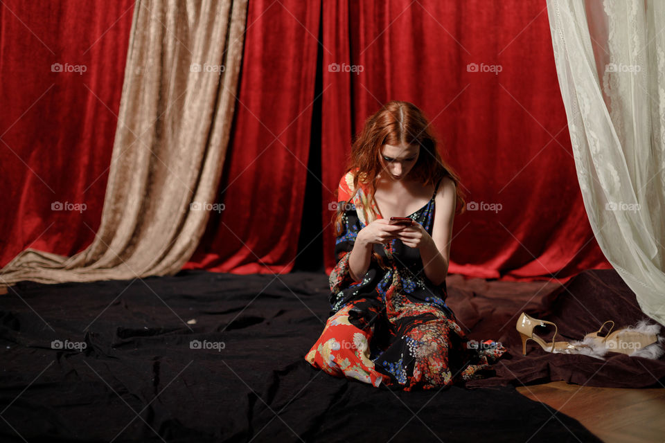 a girl with a phone on the background of a velvet curtain