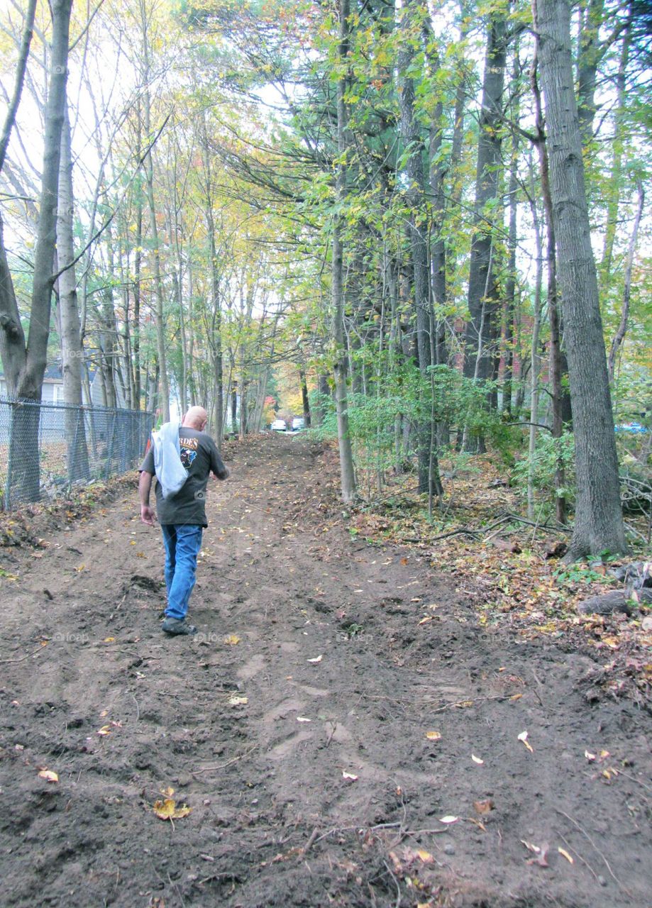 Man walking down dirt road, shirt  over shoulder.