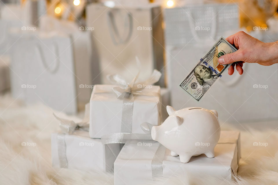 piggy bank with 100 dollars banknote in festive New Year atmosphere of scenery.  Magical bokeh with Christmas tree and bright lights.