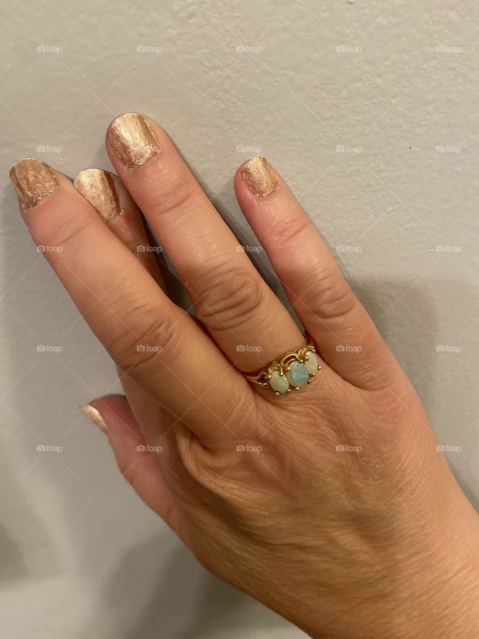 A photo of my hand with two fingers crossed and with nails painted a peachy marbled gold, white polish with a gold color on top. I’m wearing an opal ring given to me by my late Aunt Helen, who, like me, had an October birthday.