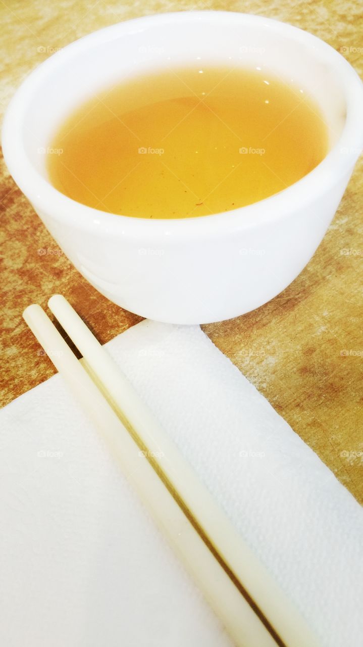 Chinese tea served in a small white teacup, along with a table napkin and a pair of chopsticks.