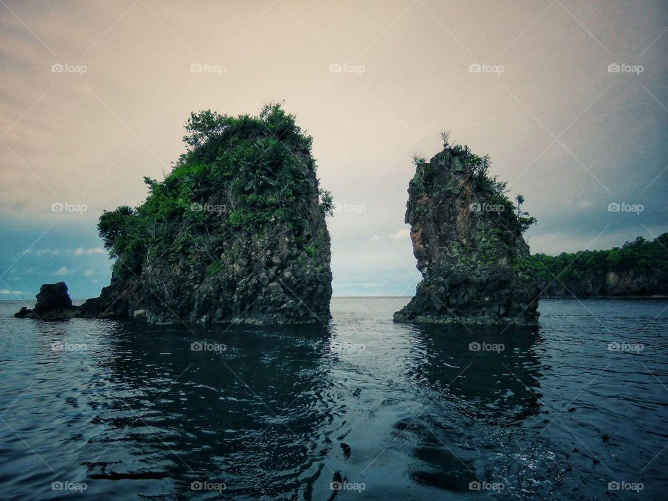 Nature landscape, two small stone islands in front of the big island hilly with green trees.