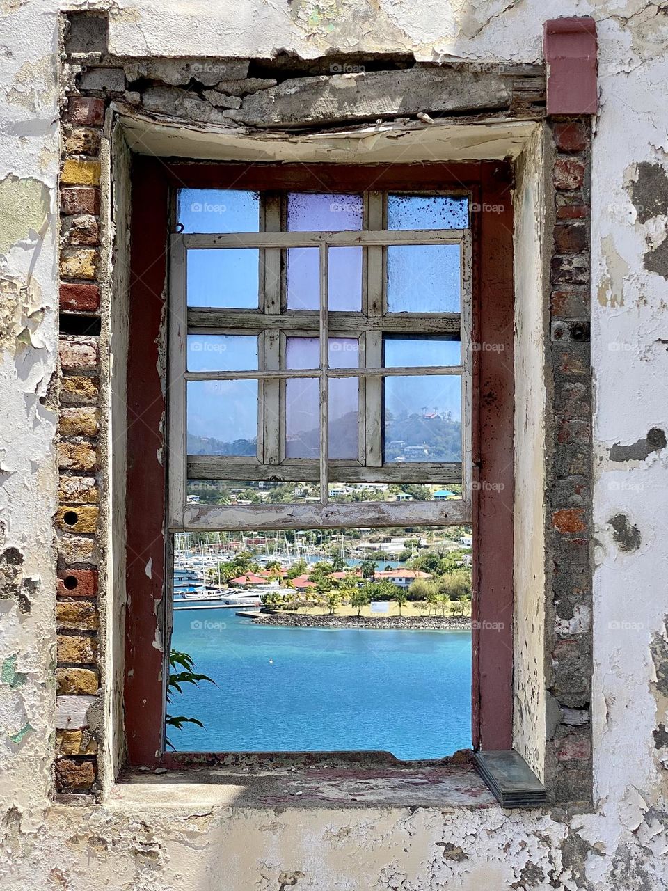 A window in an old house with a view of blue water and a town