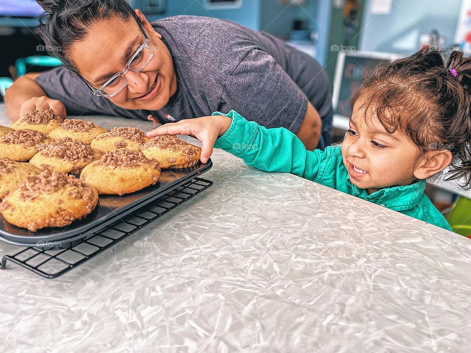 Mother and child reaching for muffins, mommy and toddler enjoying warm muffins, happy toddler and mother in the kitchen, happiness is freshly baked warm muffins, toddler and mother portraying the emotion of happiness, happy faces on mother and child