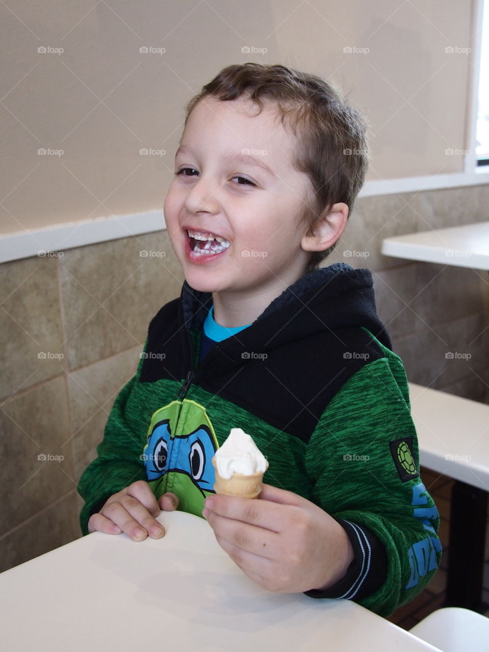 A little boy really enjoys his small vanilla cone that really hits the spot. 