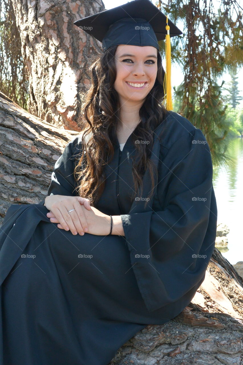 Happy graduated student sitting on tree trunk