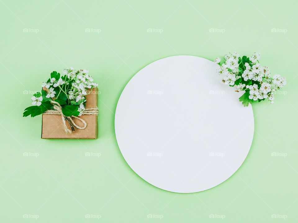 Small gift box tied with jute thread with a blossoming apple tree branch and a round empty callout on a mint background, close-up