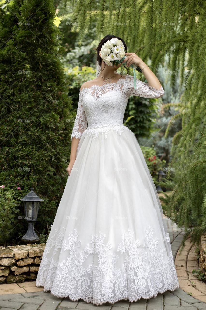 Bride in white dress hiding her face with wedding bouquet 