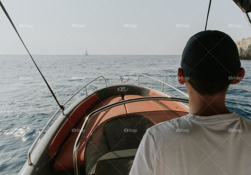 Portrait of one young Caucasian man from the back sailing on a motor boat on the sea on a sunny summer day, close-up side view.