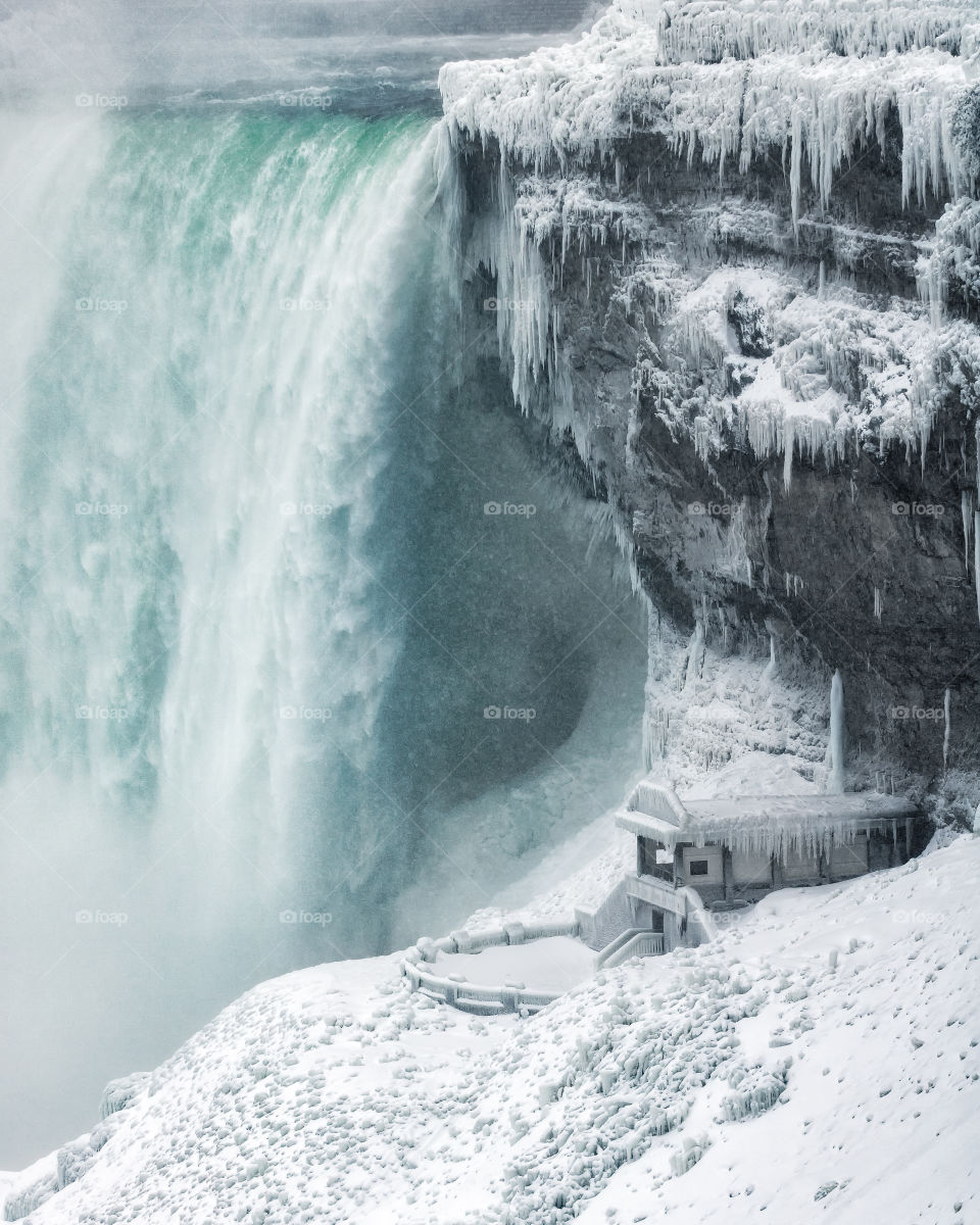 Frozen winter wonderland with a massive waterfall flowing next to a small building. Niagara Falls Ontario Canada. 