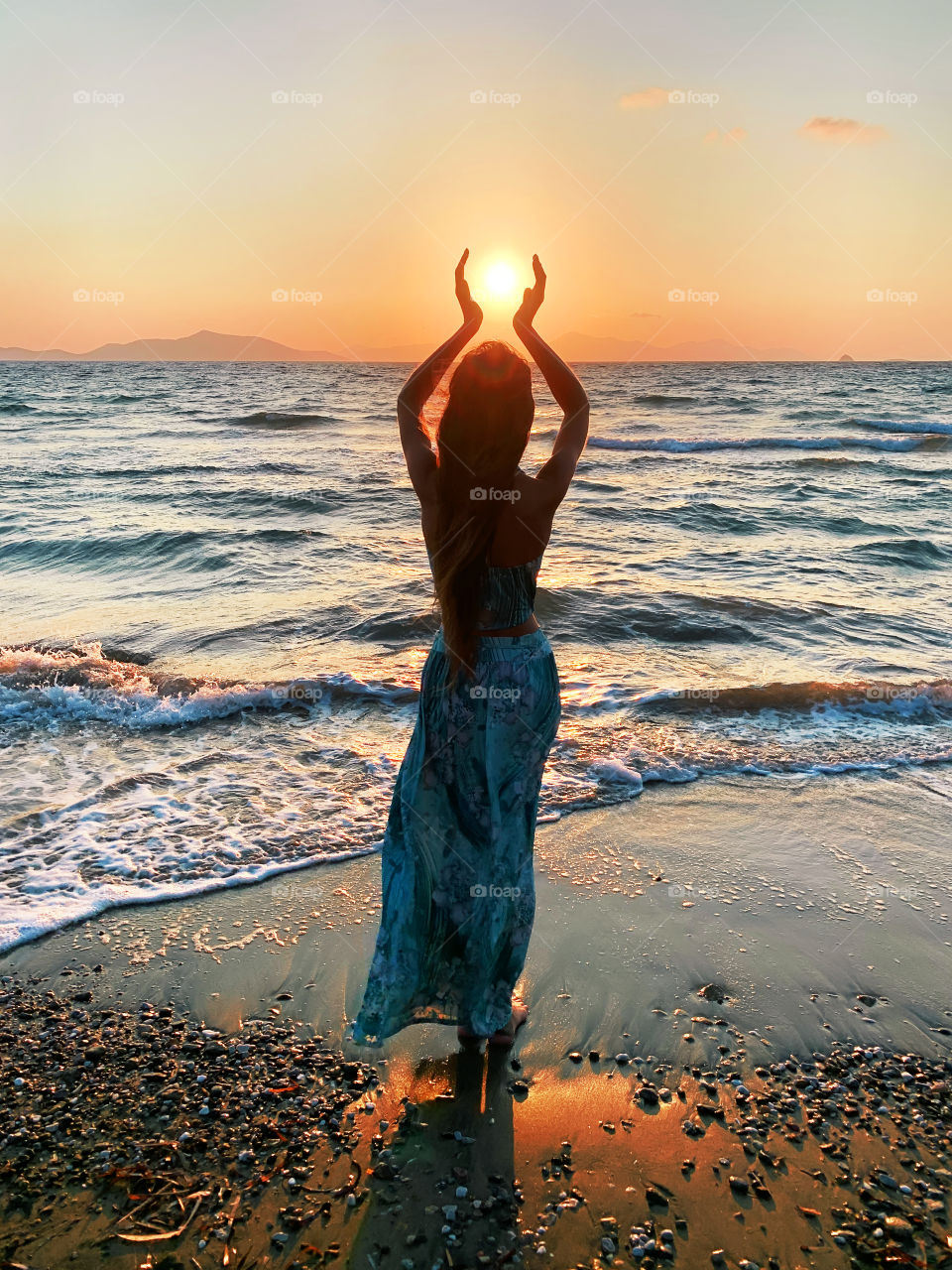 Silhouette of a young woman holding a sun at sunset over the sea 