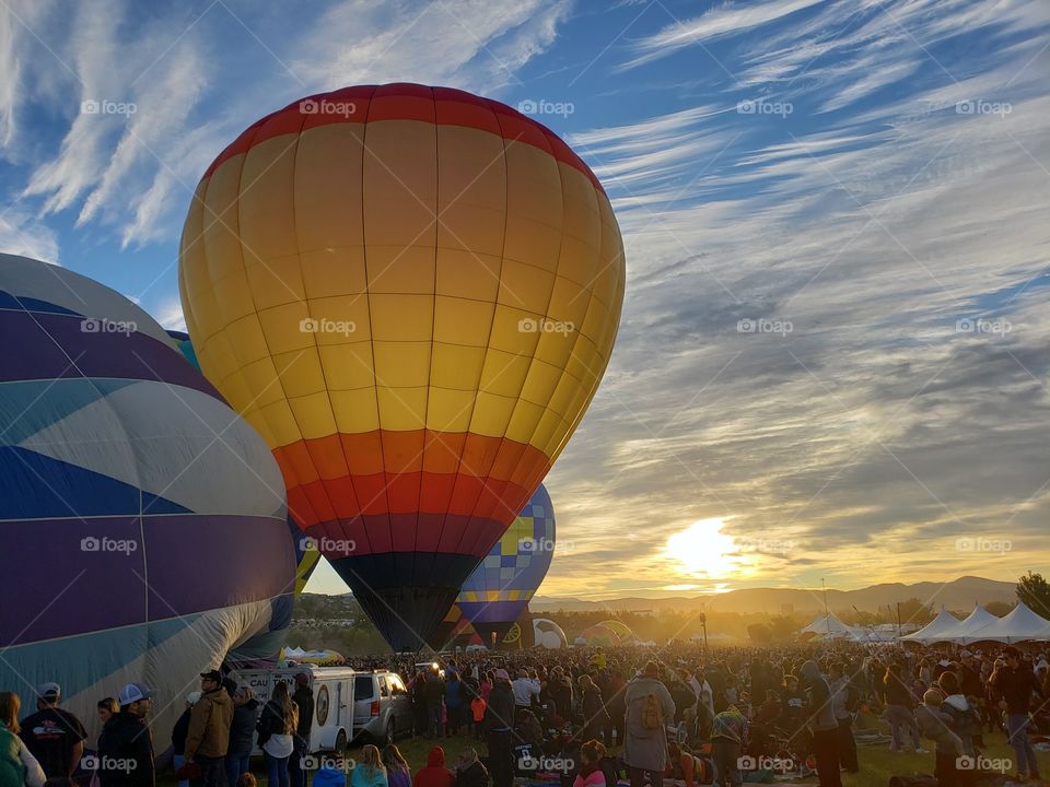Bright, colorful hot air balloons being inflated at dawn against a bright sky background