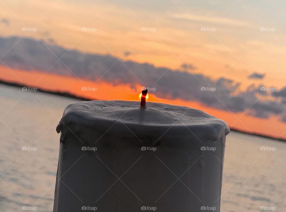 Candle Seems To Be Lit Up With A Small Flame From The Sun Setting By The Water In The Horizon.