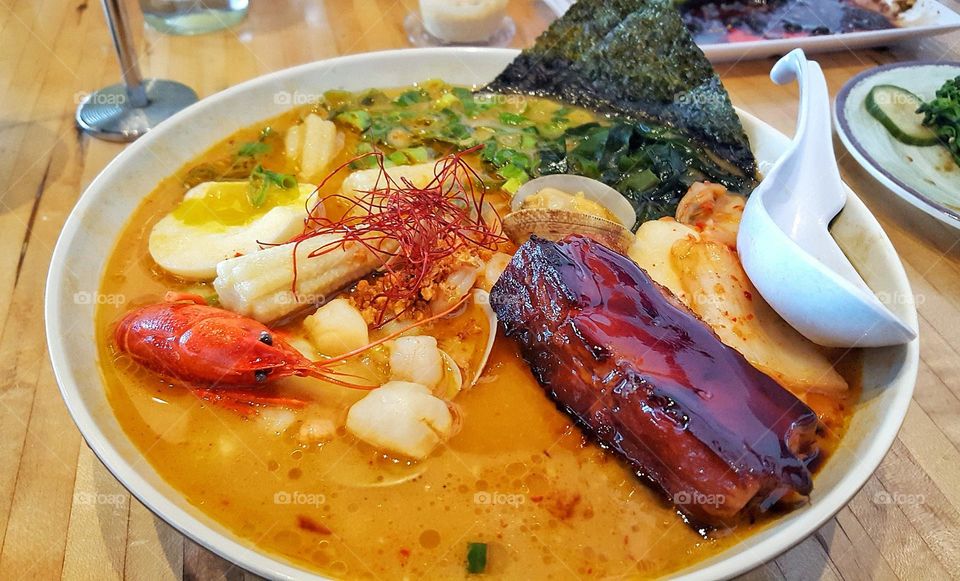 Seafood and pork belly creamy ramen with clams, nori sheet, corn, crawfish, scallops, and shrimp