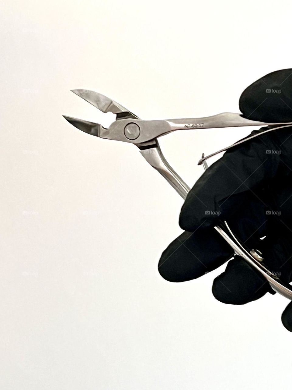 Eine Hand in einem schwarzen Nitrilhandschuh hält ein Maniküre-Werkzeug